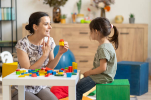 An adult Speech Therapy expert positively engages a young Child using colorful blocks, fostering Language skills and Development in a cheerful environment