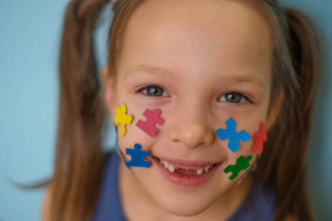 Close-up of a laughing child's face with puzzles pasted on his cheeks. The concept of autism