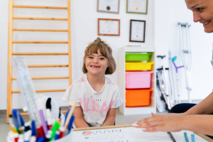A girl with down syndrome is in a classroom with her teacher,smiling and looking at camera
