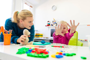Toddler girl in child occupational therapy session doing sensory playful exercises with her therapist.