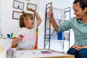 teacher and small girl with down syndrome giving high-five during art class